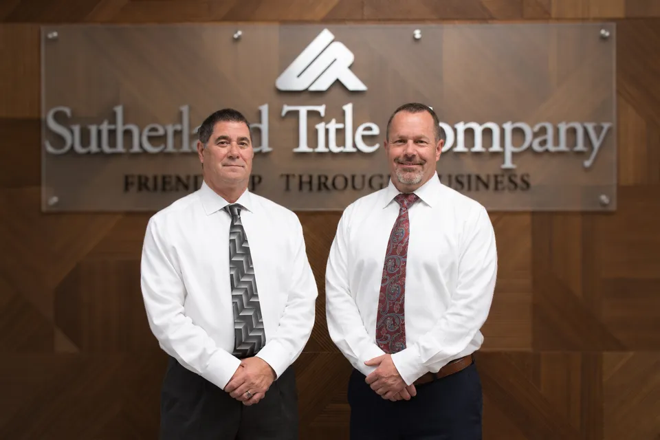 Two men standing in front of the Sutherland Title Company sign