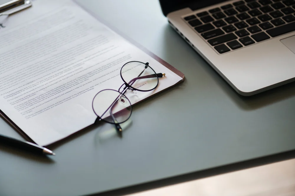 A document, glasses, and a laptop on a desk.