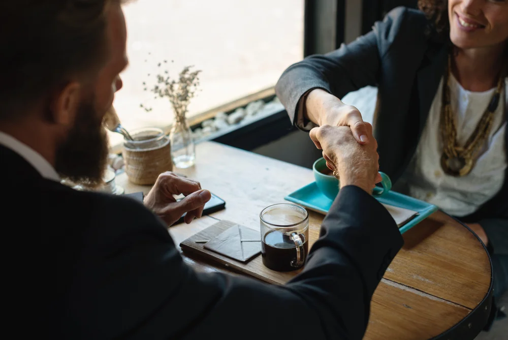 Two people shaking hands across a table.